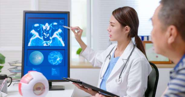 attractive young brunette ponytail female asian doctor wear white coat and stethoscope pen pointing explaining xray film on computer to gray hair old sick man at clinic - an eye model display