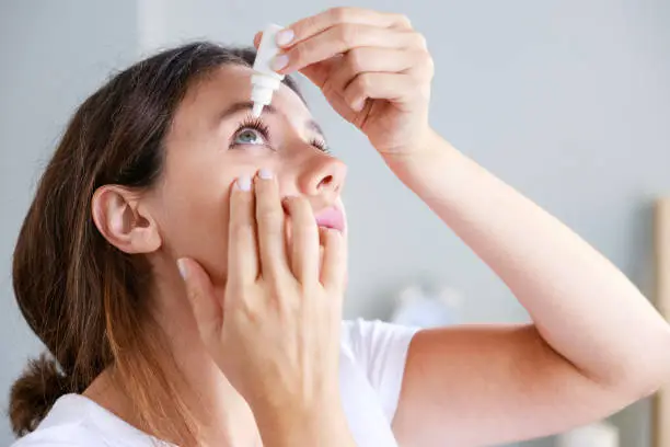 Senior woman drips eye drops into her eyes. Woman suffering from irritated eyes or eye diseases. Vision and ophthalmology medicine.